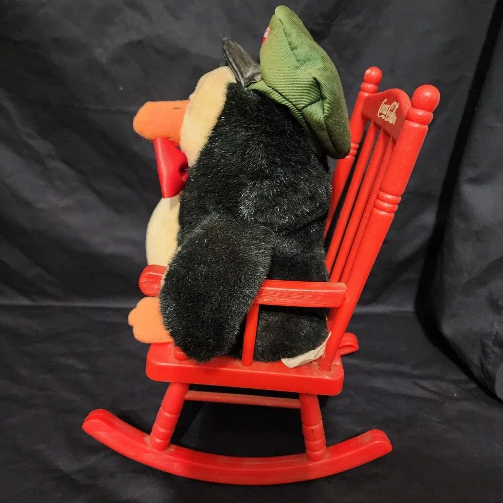 1997 vintage Coca-Cola‎ penguin plush toy sitting in a red rocking chair.